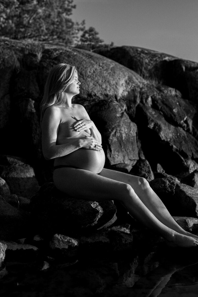 En gravid kvinna sittandes på ett berg tittar ut på vattnet