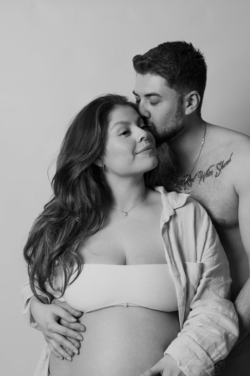 En bild på en gravid kvinna som blir omhållen av sin partner under en gravidfotografering i studio i Stockholm
