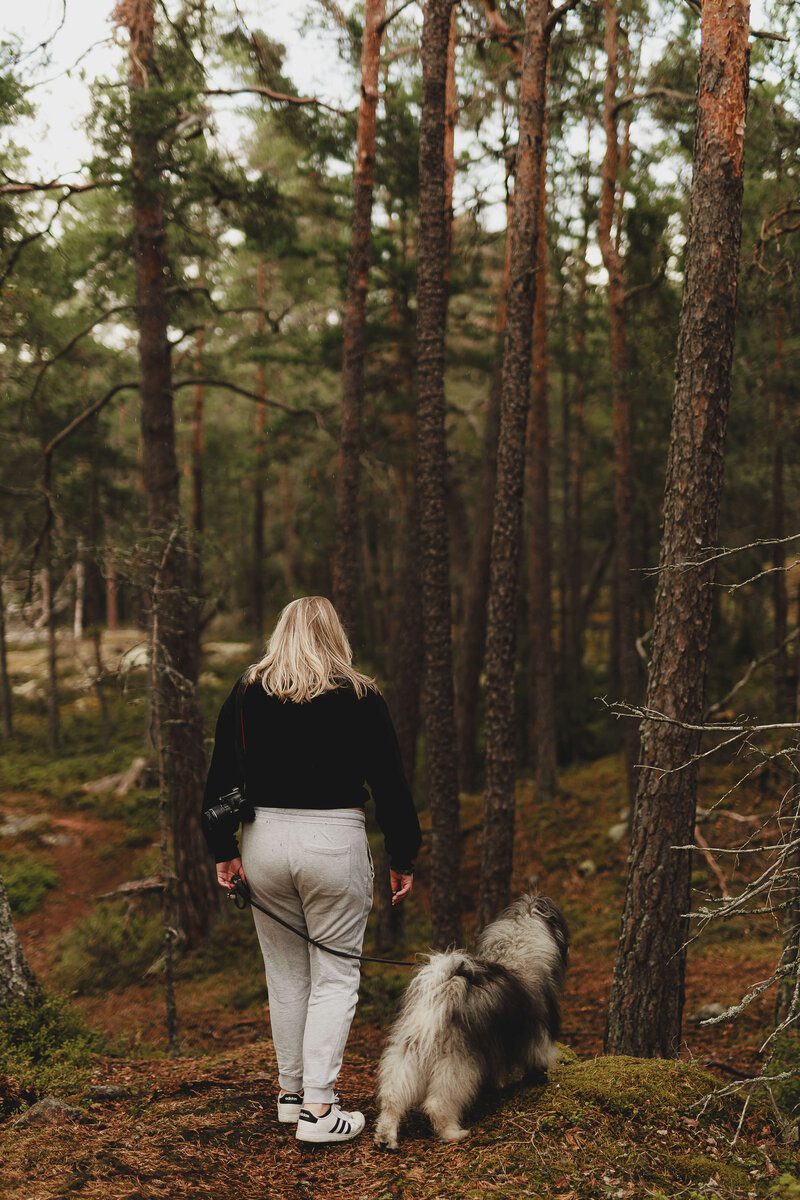En bild bakifrån på fotografen Fia Wolle tillsammans med sin hund Kito i skogen i Stockholm