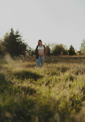 Gravidbild på en gravid kvinna gåendes i högt gräs under en gravidfotografering